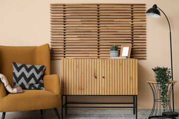 Soft armchair, wooden chest of drawers, lamp and folding screen in interior of beautiful living room