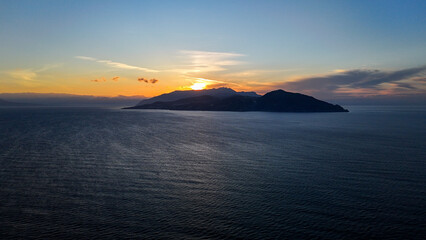 Majestic sunset over a tranquil island surrounded by serene waters and distant mountains, painted in hues of orange and purple