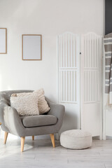 Grey armchair, houseplant, pouf and white folding screen in interior of light living room