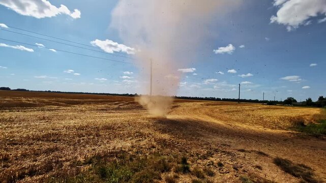A sudden dust devil, small tornado, or whirlwind sand storm blows sand and debris into the sky above a field of freshly harvested crops during a drought