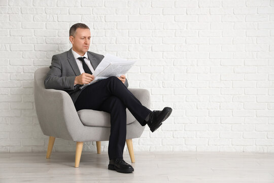 Portrait of mature businessman with modern laptop sitting on armchair near white brick wall - Powered by Adobe