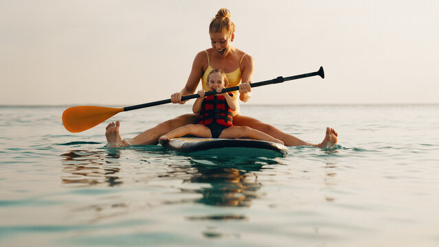 Mother teaching child to balance on paddle board during watersport activity