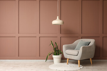 Soft grey armchair with houseplant and hanging lamp near brown wall