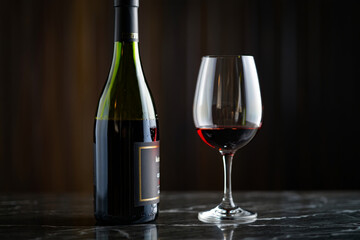 Elegant Still Life Featuring Red Wine Bottle and Glass on a Marble Surface Under Dim Lighting