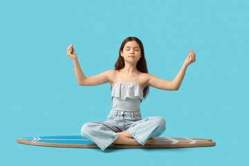 Cute girl meditating on surfboard against blue background