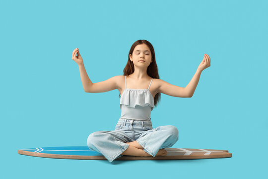 Cute girl meditating on surfboard against blue background - Powered by Adobe
