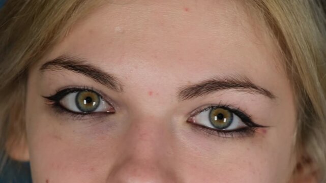 Playful young woman with defined eyes winks at boyfriend. Blonde female changes facial expression moving eyebrows expressing confusion