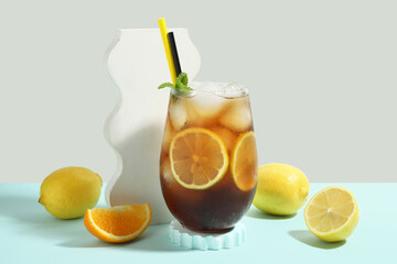 Glass of Long Island iced tea cocktail with mint and citrus fruits on blue table against grey background