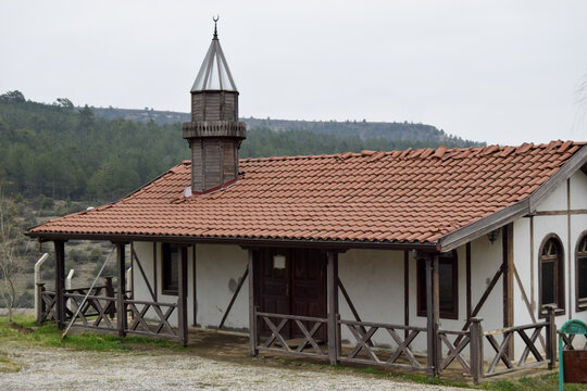 View of a quaint mosque with a red-tiled roof and wooden accents stands serenely against a backdrop of rolling hills and lush trees, Safranbolu, Karab&Atilde;&frac14;k, T&Atilde;&frac14;rkiye.