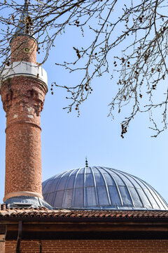 View of a striking minaret rising beside a gleaming dome against the clear blue sky, framed by the delicate tracery of bare branches, Safranbolu, Karab&Atilde;&frac14;k, T&Atilde;&frac14;rkiye.
