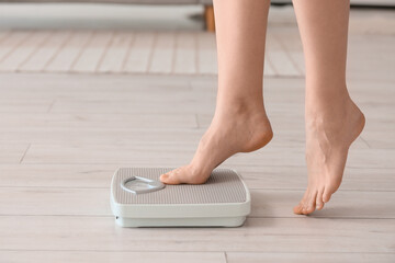 Feet of woman measuring weight on scales at home, closeup