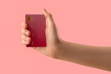 Female hand with credit card on pink background, closeup
