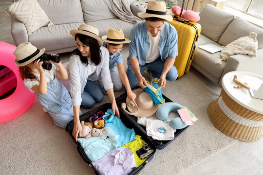 Family of tourists in summer hats packing suitcase at home - Powered by Adobe