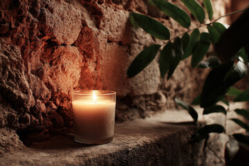 small candle flickers softly against backdrop of ancient weathered wall emitting warm inviting glow