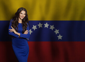 Successful young woman in blue dress smiling against flag of Venezuela background