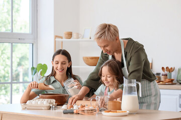 Little girl with her mother and granny rolling out dough in kitchen