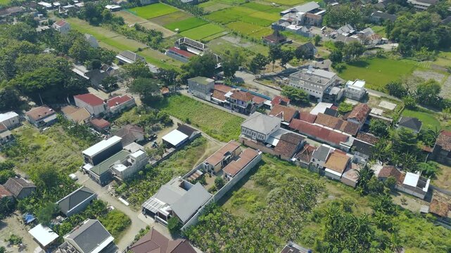 This image showcases an aerial view of a rural village, featuring traditional houses, lush greenery, and vibrant paddy fields, capturing the essence of agricultural life in a serene environment.