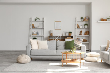 Interior of light living room with grey sofa, tables and shelf units
