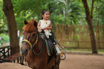 happy toddler girl riding brown horse