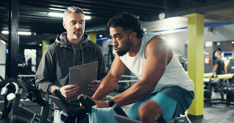 Exercise bike, man and personal trainer in gym for fitness, help or workout for health. Cycling, coach and training in sport club with stationary bicycle for spin class, cardio or wellness with flare