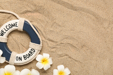 Decorative lifebuoy ring and plumeria flowers on beige sand with lines as background, closeup