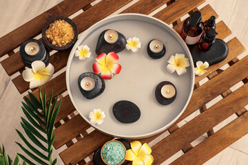 Obraz na płótnie Canvas Plate with candles, spa stones, plumeria flowers, cosmetic products and sea salt on table in salon, top view
