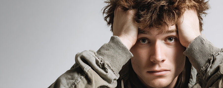 Young man expressing frustration with hands on head against a neutral background