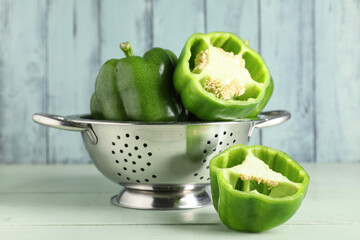 Colander with fresh bell peppers on green wooden background