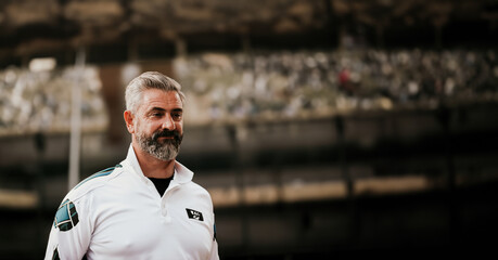 Portrait of confident mature man with gray beard wearing white polo shirt at crowded public event...