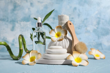 Beautiful spa composition with tray, stones, massage body brush and plumeria flowers on blue grunge background