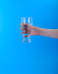 Hand holding glass of water on blue background