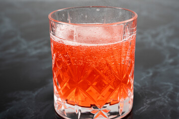 A vibrant red cocktail fills a crystal glass, sparkling with bubbles atop a smooth dark marble surface. The drink appears refreshing and inviting, perfect for any occasion.