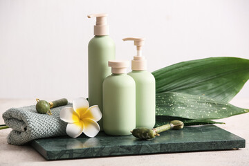 Spa composition with tray, facial massage tools, flower and bottles of cosmetic products on white grunge background, closeup