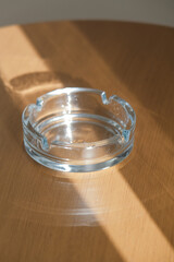 Glass transparent ash tray on brown wooden table with shadow