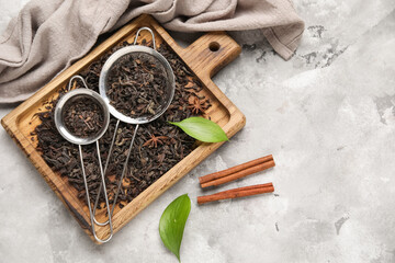 Wooden board and sieves with dry black tea leaves on grey background