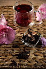 Hibiscus tea served in glass with dried flowers and fresh petals on woven mat in cozy setting