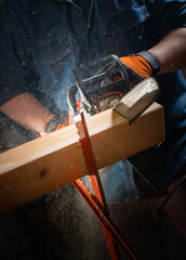 Worker uses a chainsaw to cut a plank into two pieces while working