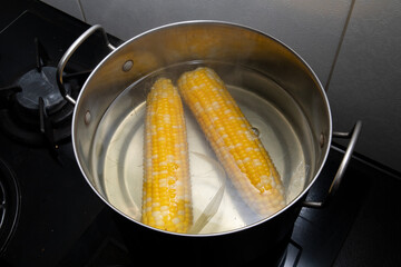 Bright yellow halves of boiled corn cobs in bubbling boiling water inside an iron pot, top view on the cooking surface. The process of cooking corn. Steamed vegetables. Vegetarianism.