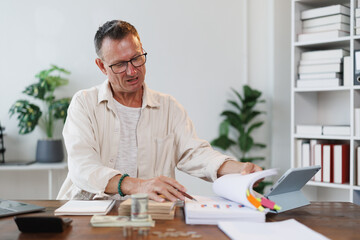 Senior accountant reviewing financial documents, analyzing charts and graphs, using tablet, calculating expenses and income, managing budget and preparing financial report in modern office