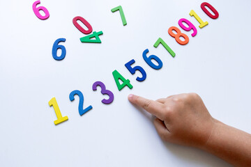 Child pointing at colorful wooden numbers on white background