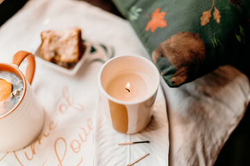 Top view of cozy setup with tea mug, candle, bread slice and fabric with handwritten lettering. Warm rustic still life in daylight.