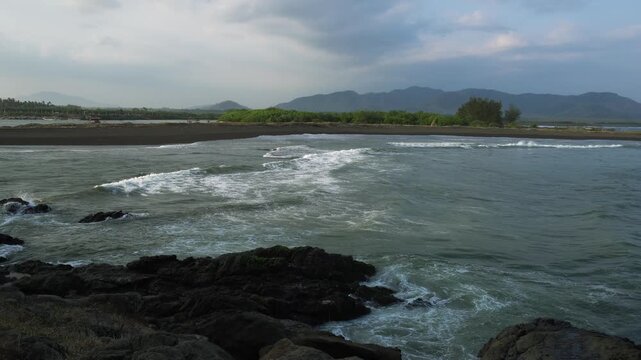 Love Bay - Teluk Love in Jember east java. A scenic view of a rocky cliff surrounded by ocean waves crashing under a blue sky. The intricate rock formations and the dynamic movement of the waves