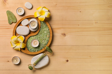 Beautiful spa composition with tray, sea salt, stones, facial massage tools and plumeria flowers on wooden background