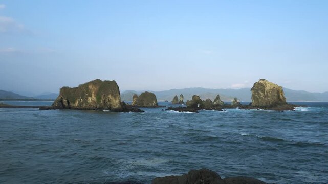 Love Bay - Teluk Love in Jember east java. A scenic view of a rocky cliff surrounded by ocean waves crashing under a blue sky. The intricate rock formations and the dynamic movement of the waves
