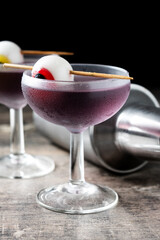Purple Halloween cocktail garnished with candy eye on wooden table