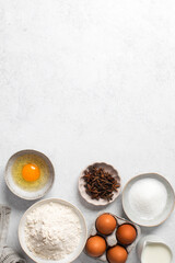 Baking ingredients flat lay with flour, eggs, sugar, and spices on marble surface. Copy space