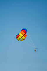 A person soars through the sky while parasailing beneath a vibrant, multicolored parachute in Bulgaria