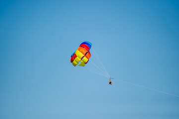 A person soars through the sky while parasailing beneath a vibrant, multicolored parachute in Bulgaria