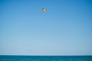 A single parasailer floats peacefully above the sea, tethered to a bright yellow parachute under a clear blue sky in Bulgaria