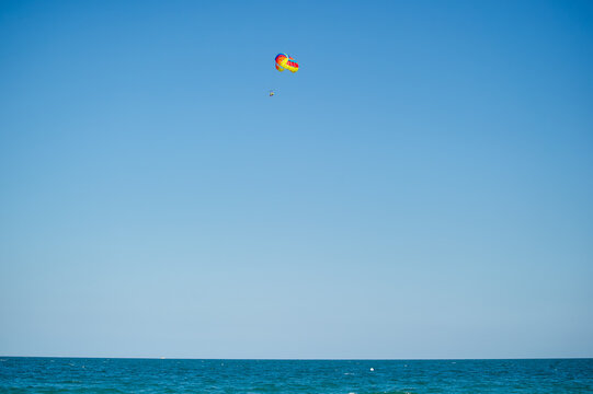 A single parasailer floats peacefully above the sea, tethered to a bright yellow parachute under a clear blue sky in Bulgaria